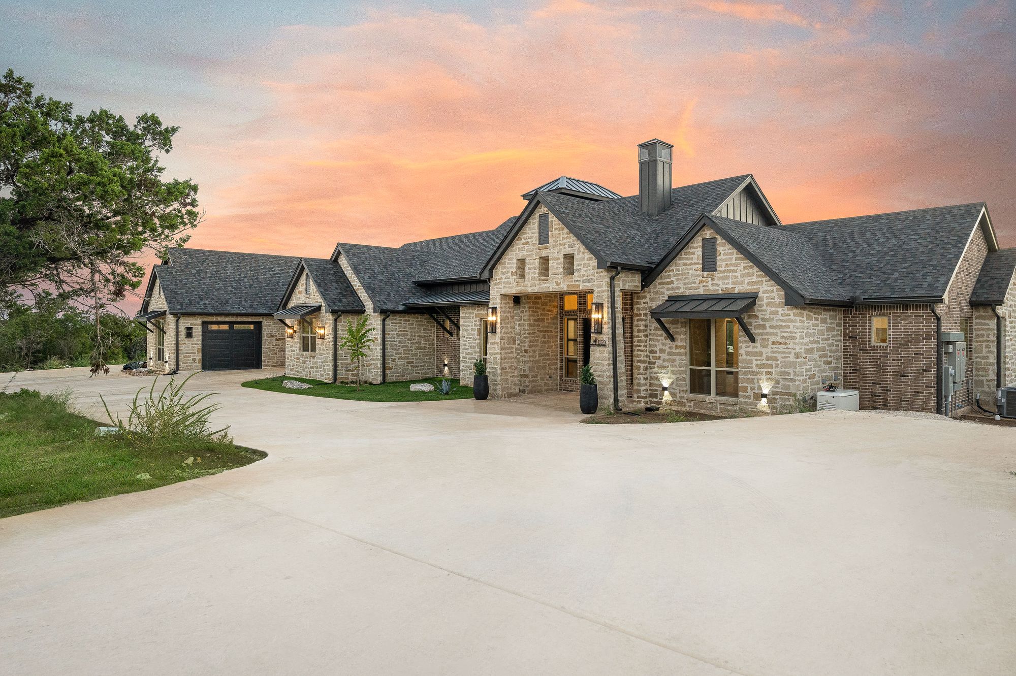 Luxury custom home estate at sunset with stone exterior and broad lawn
